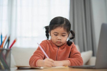 Concentrated Young Girl Writing in Notebook. A focused young girl with pigtails diligently writing in a notebook at home, with a serene look. Education for kids concept.