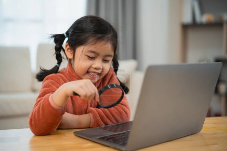 Curious Girl Exploring with Magnifying Glass and Laptop. Smiling young girl with pigtails using a magnifying glass to look at a laptop screen, showing curiosity and joy. Education for kids concept.