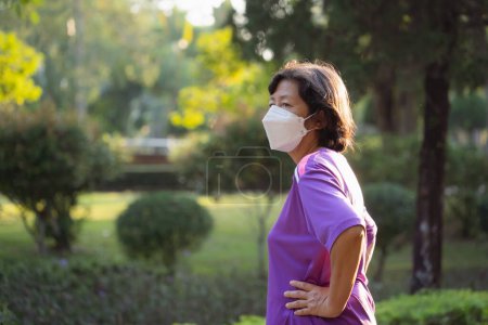 Une femme portant une chemise violette et un masque pour protéger pm 2.5 ou covid-19. Elle se tient dans un parc. Concept de prudence et de préoccupation pour la santé