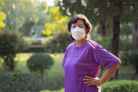 Une femme portant une chemise violette et un masque pour protéger pm 2.5 ou covid-19. Elle se tient dans un parc. Concept de prudence et de préoccupation pour la santé