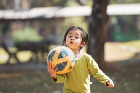 Photo for A young girl is holding a soccer ball in her hands. She is wearing a green shirt and she is excited about playing soccer - Royalty Free Image