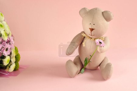 Photo pour Nounours en tissu sur un fond rose pastel avec des fleurs et un espace libre pour le texte. lumière naturelle, focalisation sélective - image libre de droit