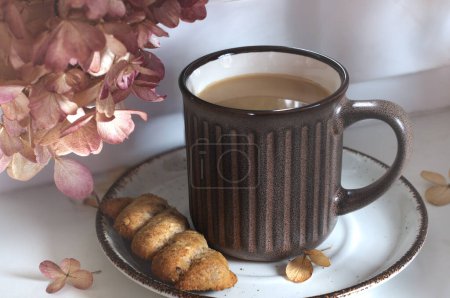 Téléchargez les photos : Tasse matinale de cappuccino avec un cookie. Fenêtre, lumière naturelle, fleurs et café. Focus sélectif - en image libre de droit