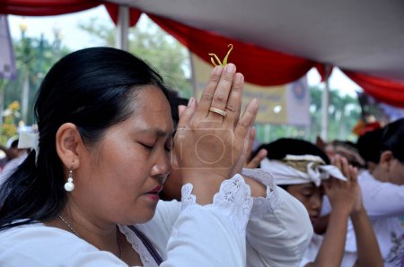 Téléchargez les photos : Bali, Indonesia - March 3, 2015 : A Hindu woman praying with a flower between her fingertips, Bali, Indonesia - en image libre de droit