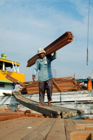 Foto de Yakarta, Indonesia - 29 de mayo de 2010: Los trabajadores transportan madera de camiones a barcos en el puerto de Sunda Kelapa, Yakarta - Indonesia - Imagen libre de derechos