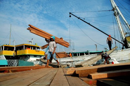 Foto de Yakarta, Indonesia - 29 de mayo de 2010: Los trabajadores transportan madera de camiones a barcos en el puerto de Sunda Kelapa, Yakarta - Indonesia - Imagen libre de derechos