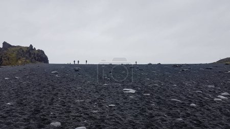 Téléchargez les photos : Les gens sur une plage de sable noir en Islande à faible angle contre le ciel gris - en image libre de droit