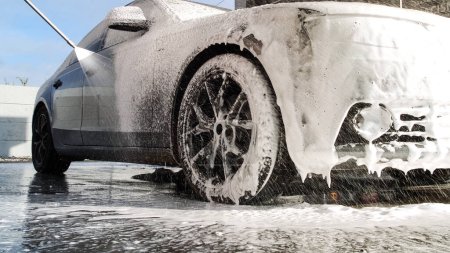Téléchargez les photos : Laver une voiture de luxe sur un lave-auto sans contact. Lavage voiture berline avec de la mousse et une eau haute pression. Nettoyage de printemps dans un lave-auto. - en image libre de droit