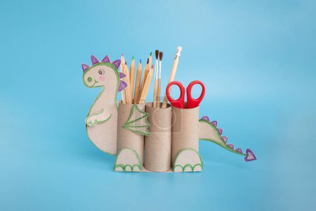 Drachen formen einen Bleistifthalter aus Toilettenpapier und einer Schere, Recyclingkonzept, DIY für Kinder, einfache Tätigkeit, blauer Hintergrund