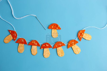 Téléchargez les photos : Une chaîne de champignons d'orange en écorce de mandarine séchée sur fond bleu, art conceptuel, automne, artisanat et activité pour les enfants, vue de dessus - en image libre de droit