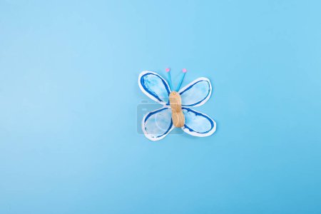 paper butterfly sitting on top of a blue surface, part of process making paper craft easy craft for kids, DIY, tutorial