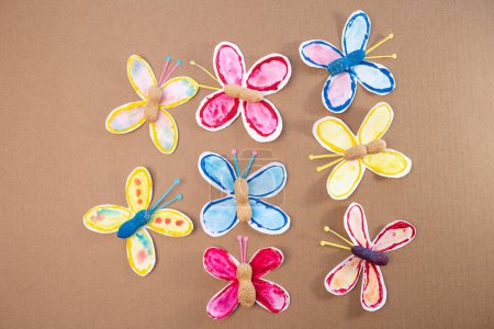 a group of paper butterflies sitting on top of a brown surface, part of process making paper craft project, stamp, paint tubes, recycling concept, easy craft for kids, DIY, tutorial
