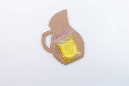 Téléchargez les photos : Un sac congélateur contenant du liquide jaune est collé à un morceau de carton d'artisanat pichet de limonade, partie du processus de fabrication, bricolage, tutoriel, projet pour les enfants, artisanat d'été facile à partir de papier recyclé, - en image libre de droit