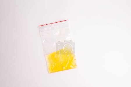 a close up of a plastic bag on a white surface, minimalism, yellow liquid inside, top view