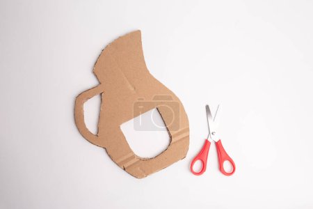 Paper cutout of pitcher with scissors, cardboard crafting materials for assembly, part of tutorial