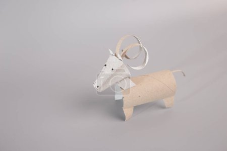DIY-Anleitung für die Herstellung entzückender Böcke oder gehörnter Rinder aus recycelten Toilettenpapierrollen. Ideal für Kinder und Kindergärtner, fördert Kreativität und Feinmotorik, Figur auf grauem Untergrund