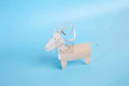 Photo for Engaging toilet paper roll craft concept featuring a homemade animal paper craft tutorial for kids and kindergartens. Create your own ram, ibex, or goat toy with ease.Curled-Horn creature on blue - Royalty Free Image