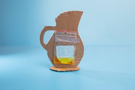 a plastic bag attached to cut out of cardboard, pitcher craft made of cardboard, part of tutorial, blue background