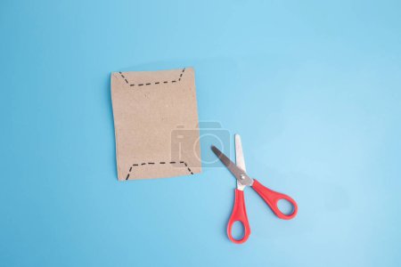 Crafting Essentials: Pair of scissors beside a piece of paper on blue surface. Back shot of card template for craft projects