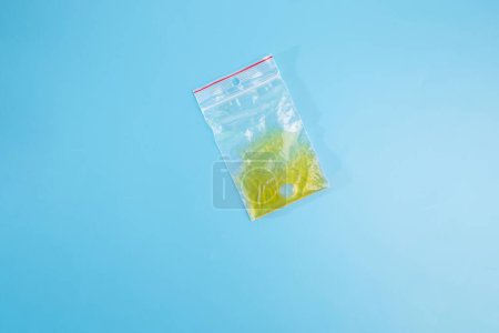 minimalism, featuring a plastic bag placed delicately on a blue surface. From the top view, the yellow liquid enclosed within the bag offers a captivating focal point, color, part of crafting process