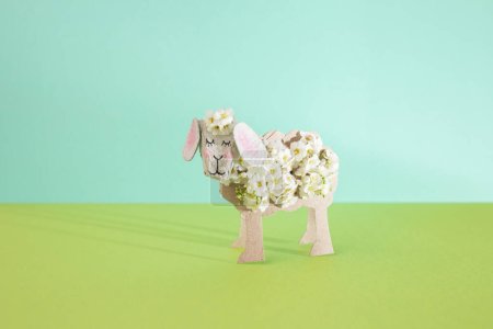 Artesanía de ovejas de primavera hecha de papel higiénico reciclado y pequeñas flores blancas, perfectas para niños pequeños, fondo verde, vista frontal,
