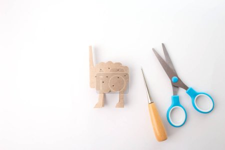 a carton body blank, a cutout used for crafting, placed on a white surface next ot scissors and awl part of a crafting process. sheep project, simple spring activity for kids, tutorial, 