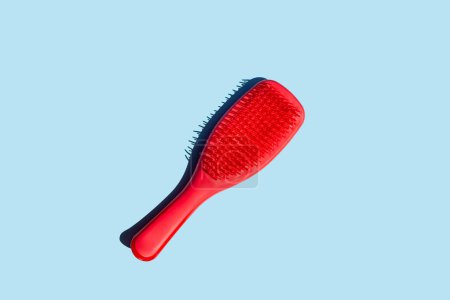 Vividly contrasting blue and red hues captivate in a top-down view of a comb. Against a clean background, the dynamic interplay of colors adds a modern flair to the timeless concept of hair grooming.