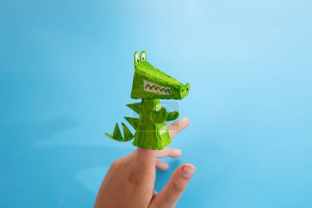 Kids handmade finger toy, crocodile paper craft. Recycled paper materials, green crocodile design with teeth and spikes. Fun and eco-friendly, great for childrens creative projects and playtime.