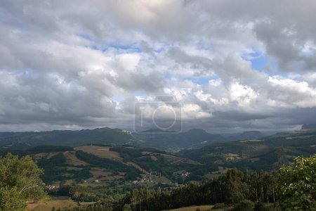 Foto de Rustic mountain landscape with cloudy sky.Bien Aparecida, Cantabria, meadows, trees and pastures for animals, rustic houses, sky with storm clouds. - Imagen libre de derechos