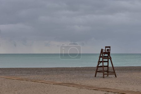 Foto de Wooden lifeguard chair on lonely beach. Cloudy sky, sandy beach, sky with storm clouds, turquoise sea, - Imagen libre de derechos