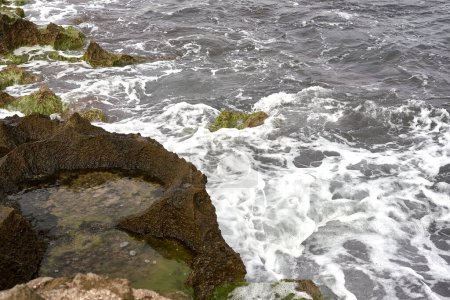 Foto de Serenity by the Seashore: AI-Crafted Coastal Harmony.Capturando detalles de una playa tranquila, pequeñas olas rompiendo suavemente con rocas cubiertas de algas. El agua, ligeramente agitada, refleja una costa serena - Imagen libre de derechos