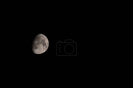 Photo for Nocturnal Shift: Waning Moon on the Left.Telephoto lens captures the waning moon shifted to the left against the black nocturnal sky, highlighting vast empty space - Royalty Free Image