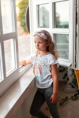 Foto de Hermosa niña en ropa de verano de moda se encuentra cerca de la ventana - Imagen libre de derechos