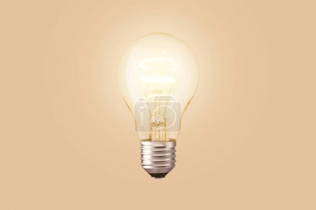 Foto de La bombilla brilla sobre un fondo beige. Tecnología y ciencia - Imagen libre de derechos
