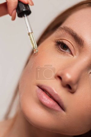 Photo for Beautiful redheaded fresh girl holding a dropper and dripping oil on her face. Beauty and skin care - Royalty Free Image
