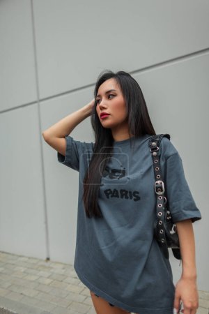 Beautiful fashion young Vietnamese girl model in stylish urban clothes with T-shirt, shorts and leather bag on the street. Pretty cool girl