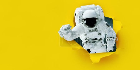 L'astronaute de l'espace déchire le papier du trou, concept. Bannière jaune pour le design et le texte. Idée créative. Voyage dans l'espace