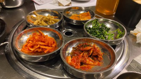 una mesa con banchan coreano muchos tazones de comida, incluyendo zanahorias y cebollas guarnición comida coreana