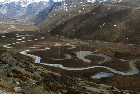 Foto de Una vista panorámica de agua pequeña que fluye en un lago en zig-zag debajo de las montañas se ve fascinante en el valle de Phalung a 16500 pies de altitud en el norte de Sikkim, India. Esta es la zona remota de Sikkim donde solo yak y ovejas se queda aquí. - Imagen libre de derechos