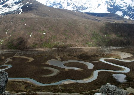 Foto de Una vista panorámica de agua pequeña que fluye en un lago en zig-zag debajo de las montañas se ve fascinante en el valle de Phalung a 16500 pies de altitud en el norte de Sikkim, India. Esta es la zona remota de Sikkim donde solo yak y ovejas se queda aquí. - Imagen libre de derechos