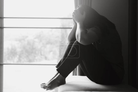 Foto de Esquizofrenia con concepto de depresión solitaria y triste en salud mental. Mujer deprimida sentada contra el suelo en casa con cuarto oscuro sintiéndose miserable. Las mujeres están deprimidas, temerosas e infelices. - Imagen libre de derechos