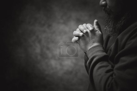 Foto de Hands folded in prayer on in church concept for faith, spirituality and religion, man praying in the morning. man hand with praying god. Person Christian men who have faith in Jesus worship in dark. - Imagen libre de derechos