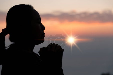 Téléchargez les photos : Faith of christian concept. Spiritual prayer hands over sun shine with blurred beautiful sunset background. Female hands worship God with love and faith. silhouette of a woman praying with a cross. - en image libre de droit