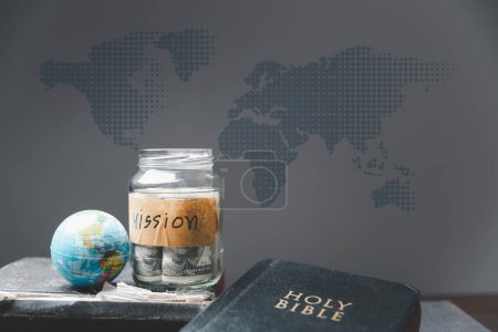 Spardosen voller Geld und Globus mit der Heiligen Bibel für Mission, christliche Mission. Bibel und Buch auf Holztisch, christlicher Hintergrund für großen Auftrag oder Earth Day-Konzept.