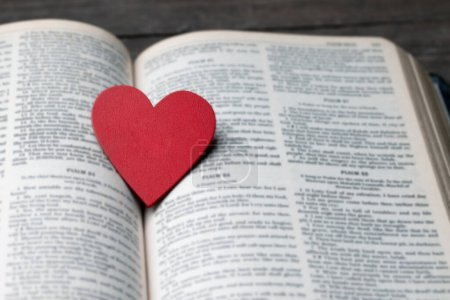 Das rote Herz auf dem heiligen Bibelbuch ist das Symbol der Liebe Gottes. Gott schenkt allen Menschen Liebe. Wir können die Bibel in der Kirche sehen oder finden. Die Bibel ist die christliche Religion. Zwei Herzen auf Seite.