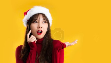 Téléchargez les photos : Young asain woman in red sweatshirt wearing santa hat posing surprised on yellow background. Merry Christmas. - en image libre de droit