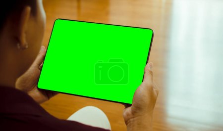 Imagen burlona de hombre asiático sosteniendo tableta digital negra con pantalla verde en blanco en casa u oficina.