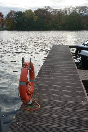 A orange lifebuoy hangs from a pole at the Spree River pier. A lifebuoy is a life-saving buoy designed to be thrown to a person in water. Berlin, Germany 