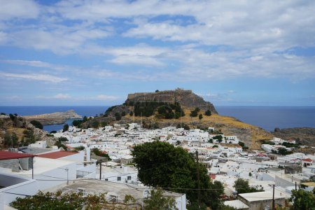 View of the white buildings of Captains houses of the 16th-18th centuries and the ancient Acropolis of Lindos in August. Lindos is an archaeological site, a fishing village and a former municipality on the island of Rhodes, in the Dodecanese, Greece.