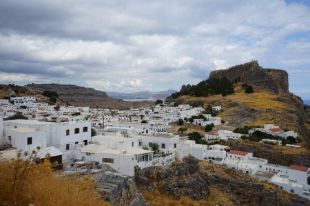 View of the white buildings of Captains houses of the 16th-18th centuries and the ancient Acropolis of Lindos in August. Lindos is an archaeological site, a fishing village and a former municipality on the island of Rhodes, in the Dodecanese, Greece.
